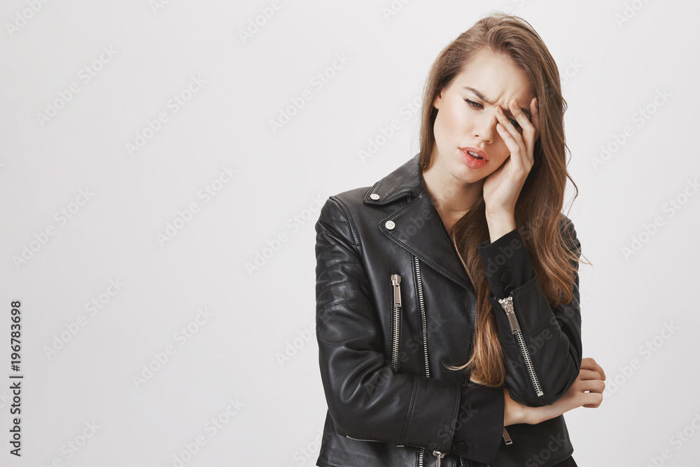 Tired woman feeling bad after working all day without break. Portrait of tired good-looking female in leather jacket holding hand on forehead, frowning, looking down with sick look, feeling headache Tired woman feeling bad after working all day without break. Portrait of tired good-looking female in leather jacket holding hand on forehead, frowning, looking down with sick look, feeling headache