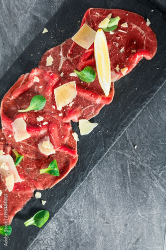 Foto Top view of the raw beef carpaccio with parmesan cheese on a black shale service board