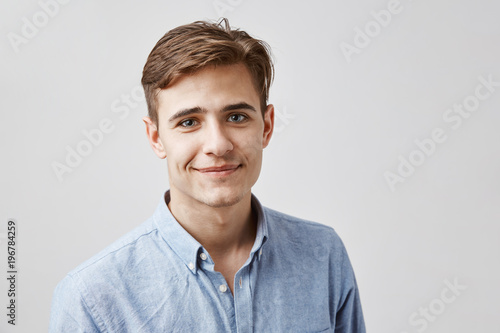 Happy young boy smiling to the camera wearing blue casual shirt, a little bit shy and unconfident talking to attractive girl he wants to ask for a date. photo