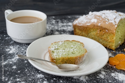 Mint cake sprinkled with powdered sugar on dark surface with coffee cup