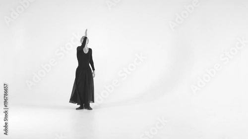 Black and white image. Young woman choreographer dancing in a black suit against a white wall background. Modern dance 4k
