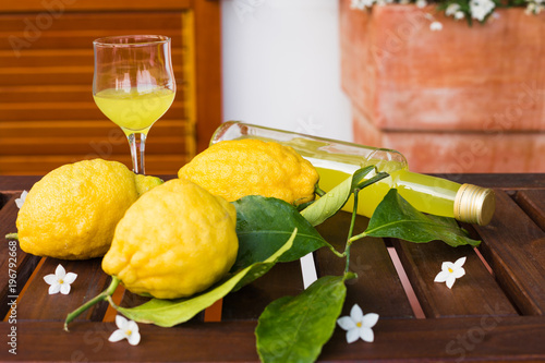 Lemonade or limoncello in a glass bottle, glass, lemons with leaves on a serving table on the terrace