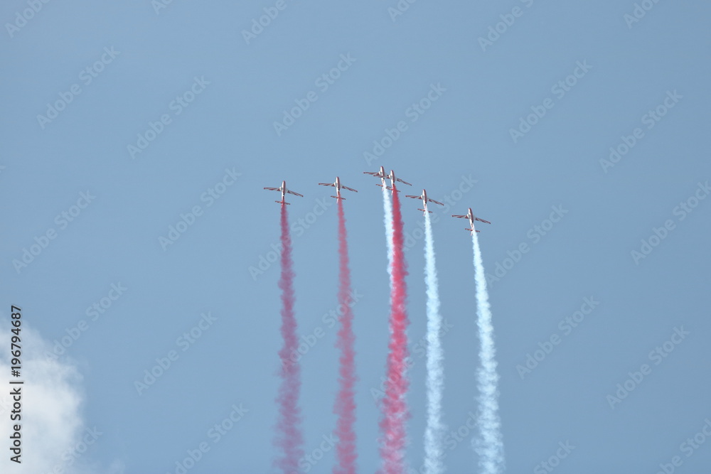 Grupa samolotów akrobacyjnych w powietrzu, leci ostro do góry zostawiając za każdym z nich biały i czerwony dym, niebieskie niebo - obrazy, fototapety, plakaty 