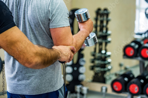 Back view man trains biceps with trainer in gym