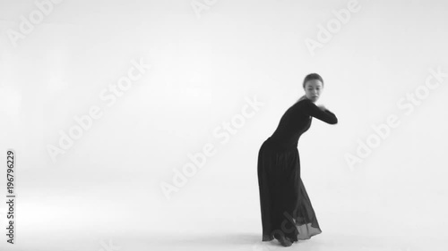 Black and white image. Young woman choreographer dancing in a black suit against a white wall background. Modern dance 4k