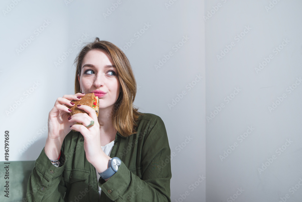 A cute girl with a sandwich in her hands looks to the side. A girl dishes a sandwich against a gray wall background A cute girl with a sandwich in her hands looks to the side. A girl dishes a sandwich against a gray wall background