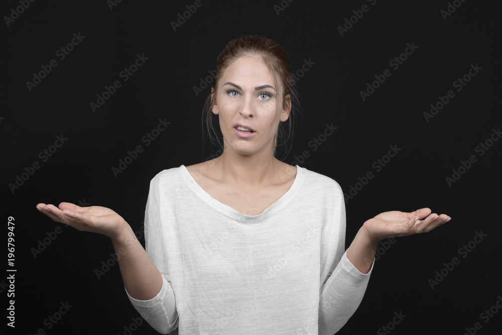 Young blond woman with arms out shrugs shoulders on black background Young blond woman with arms out shrugs shoulders on black background