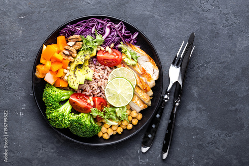 Obraz na plátne Buddha bowl dish with chicken fillet, brown rice, avocado, pepper, tomato, broccoli, red cabbage, chickpea, fresh lettuce salad, pine nuts and walnuts