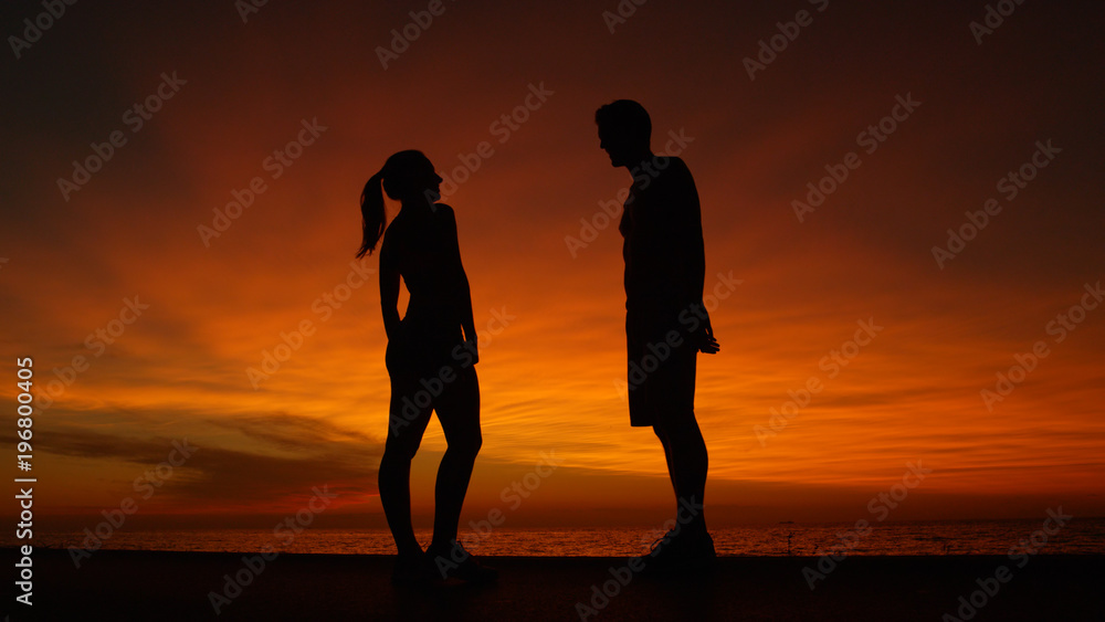 LOW ANGLE: Boyfriend and girlfriend talking at the beach at orange sunrise.