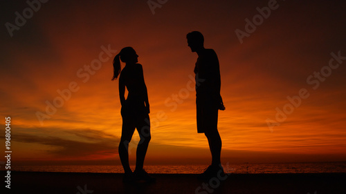 LOW ANGLE  Boyfriend and girlfriend talking at the beach at orange sunrise.