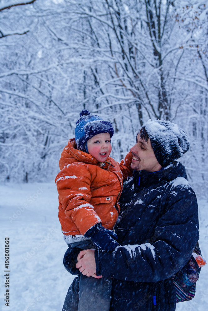 Fototapeta premium Father and his son playing outside, winter forest on the background, snowing, happy and joyful