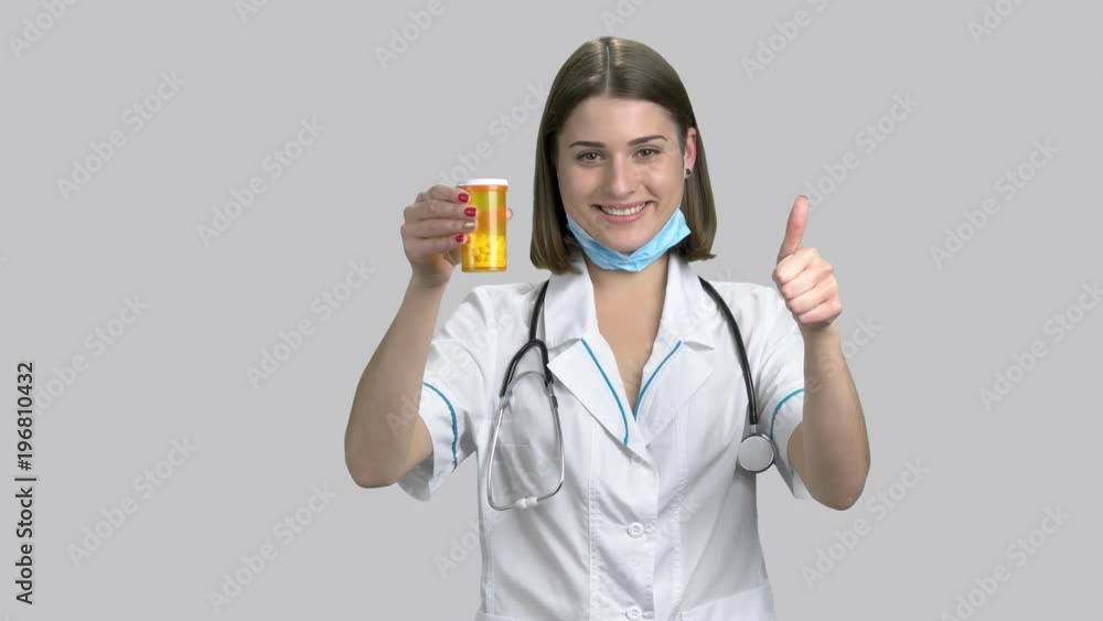 Doctor holding a bottle of prescription drugs. Beautiful caucasian doctor holding pills and giving humb up sign on gray background. Doctor holding a bottle of prescription drugs. Beautiful caucasian doctor holding pills and giving humb up sign on gray background.