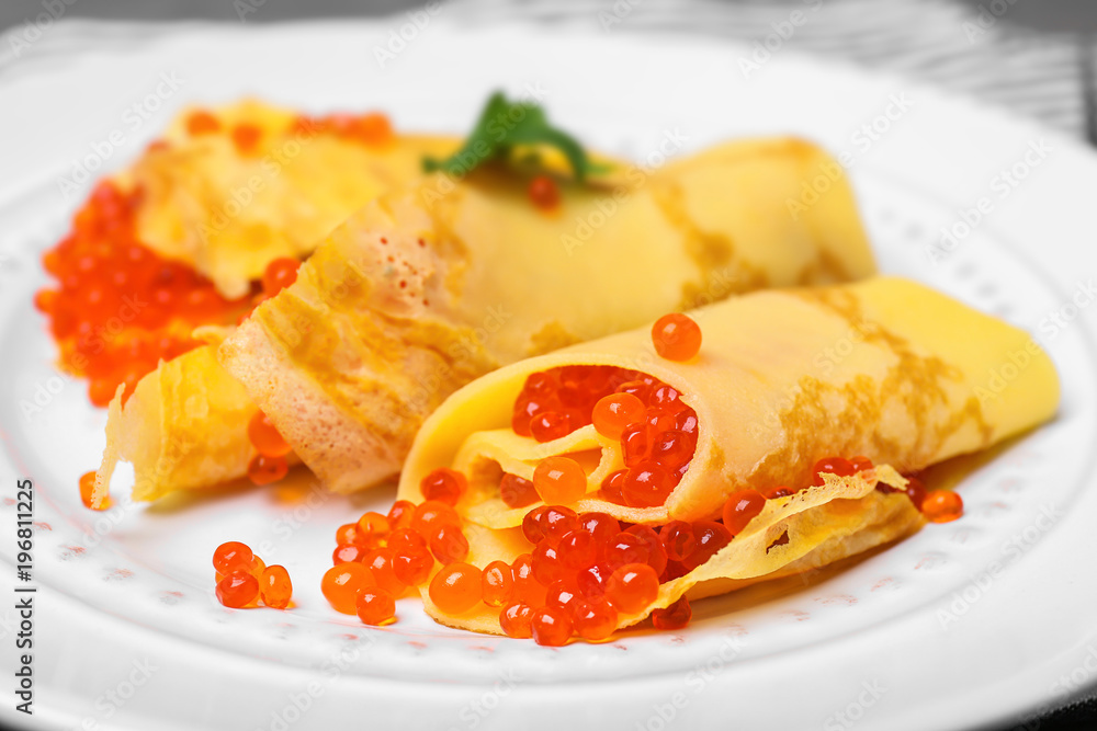 Thin pancakes with delicious red caviar on plate, closeup