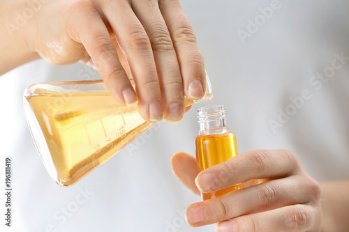 Woman pouring perfume oil into glass bottle, closeup