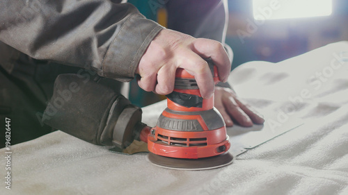 Close-up of a manual sander controlled by a worker at the factory and sanding a metal part