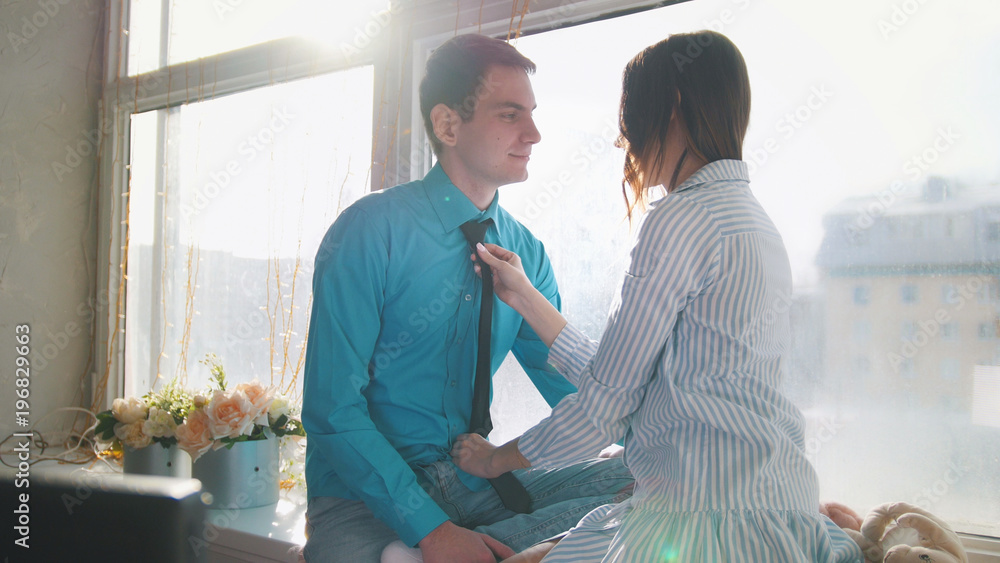 Obraz premium Young happy couple sitting on the windowsill, laughing, flirting, plauing