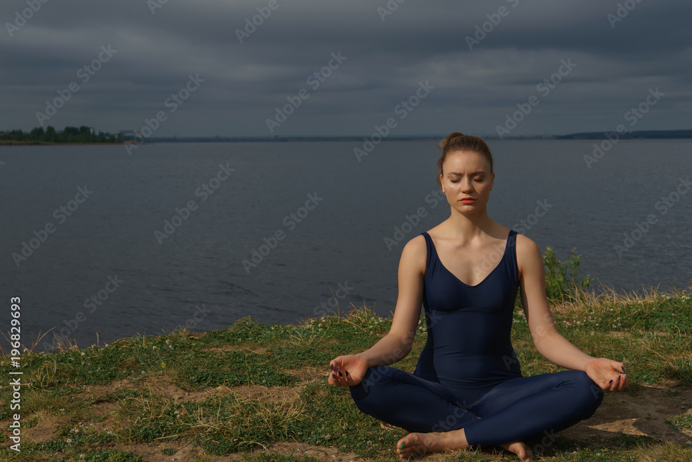 Fototapeta premium Young girl in blue sportswear meditating outdoor