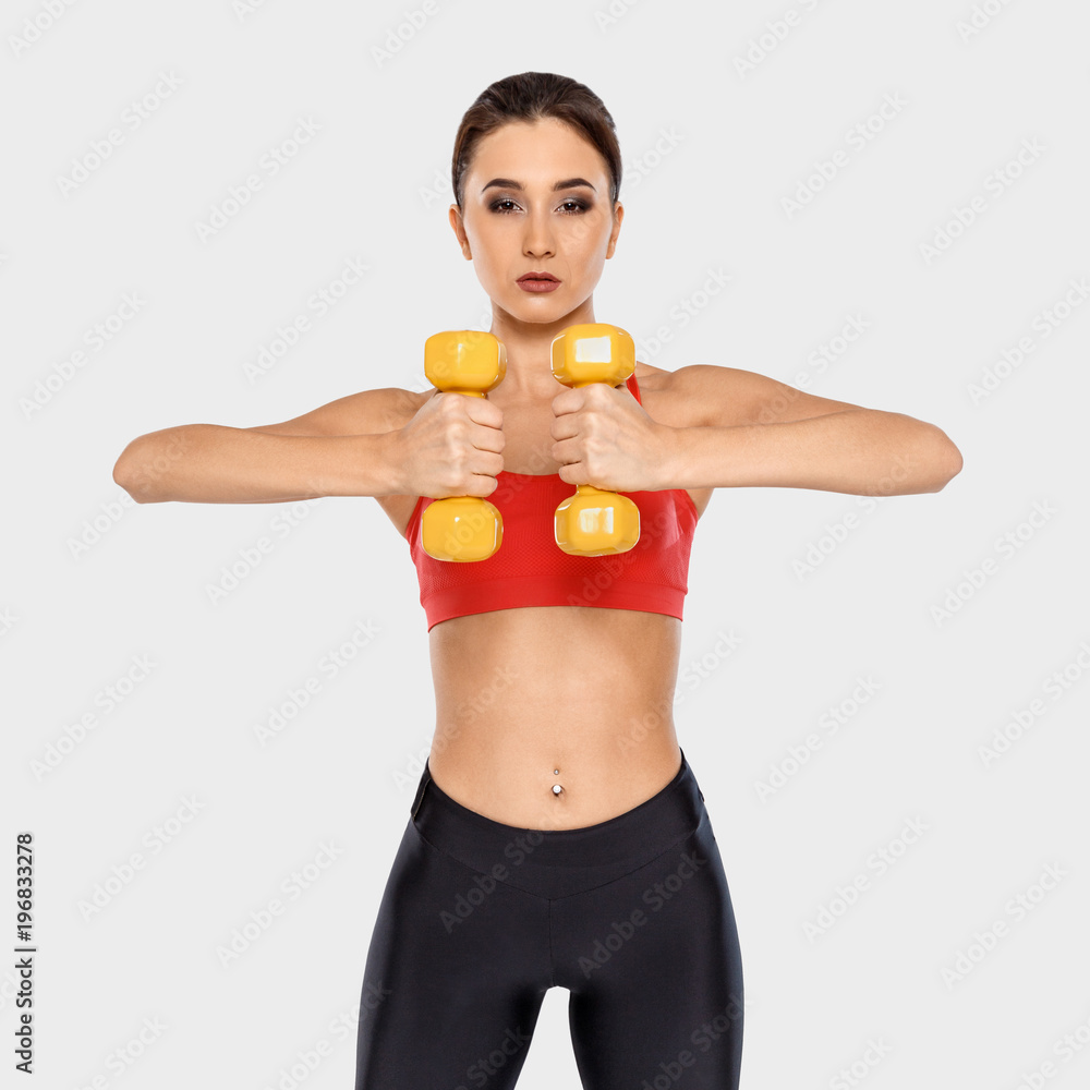 A sporty girl in a red T-shirt is holding dumbbells at the chest level A sporty girl in a red T-shirt is holding dumbbells at the chest level