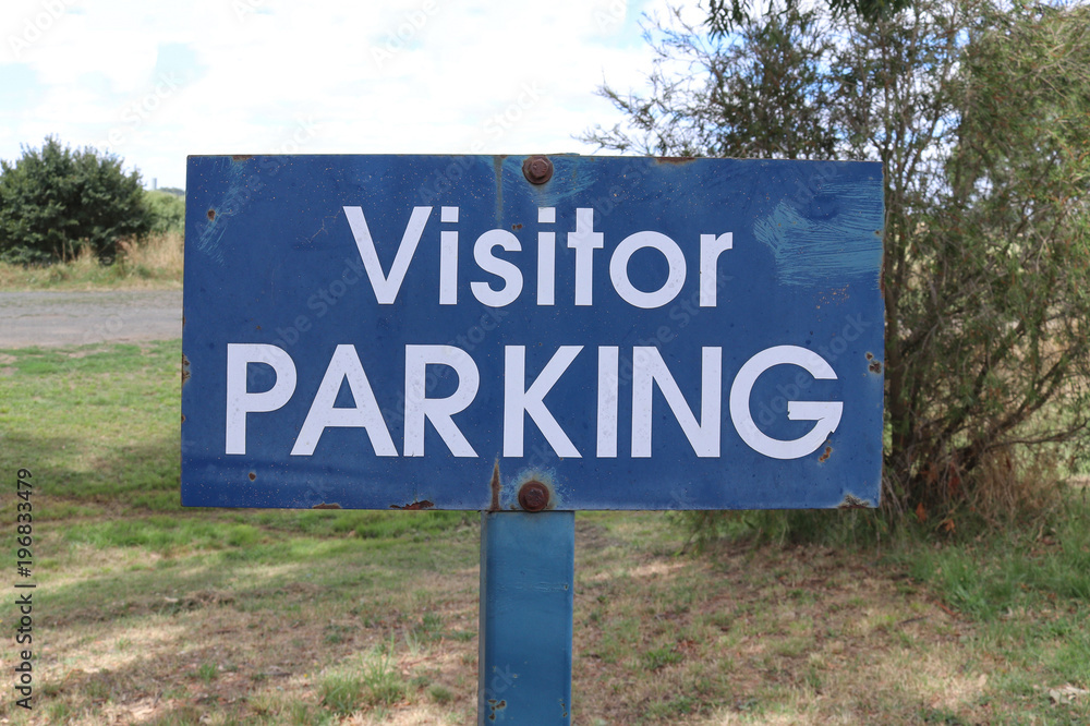 a weathered metal blue and white Visitor Parking sign