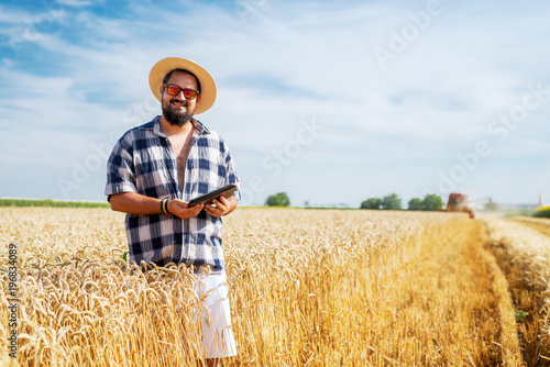Smiling bearded man standing in the field on a sunny day and looking into a camera.