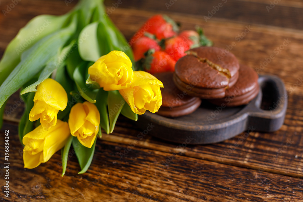 Yellow tulips, biscuits and strawberries on a wooden table. A nice gift for your beloved. A bouquet of tulips and a treat. Yellow tulips, biscuits and strawberries on a wooden table. A nice gift for your beloved. A bouquet of tulips and a treat.