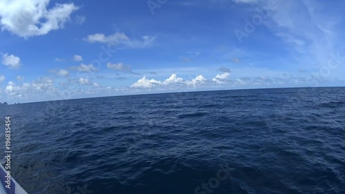 POV wide shot: yacht moving by clear sea water, bright sunny day on island