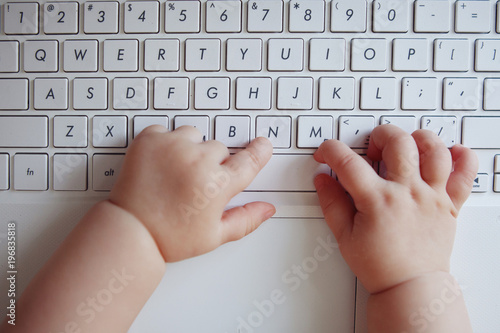 Foto Small plump baby pens on the white keyboard of the laptop typing fingers text
