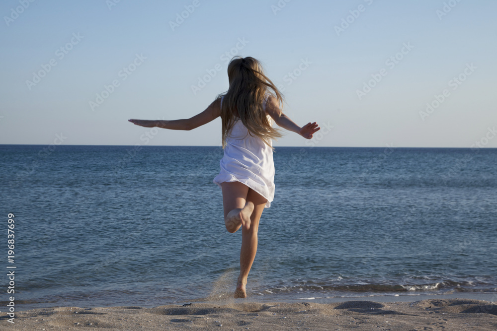 Teen girl in a white sundress running on sand. Back view