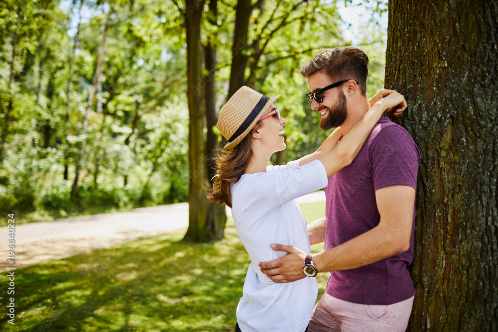 Naklejka premium Young couple embracing and leaning against a tree in the park