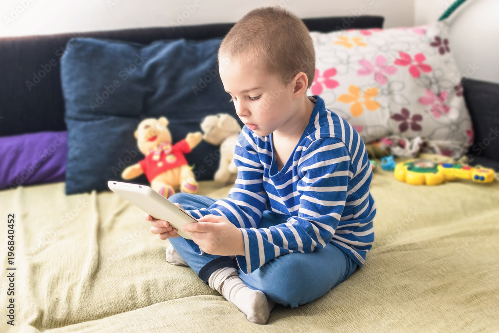 Cute boy sitting on bed while playing with tablet at home. Cute boy sitting on bed while playing with tablet at home.
