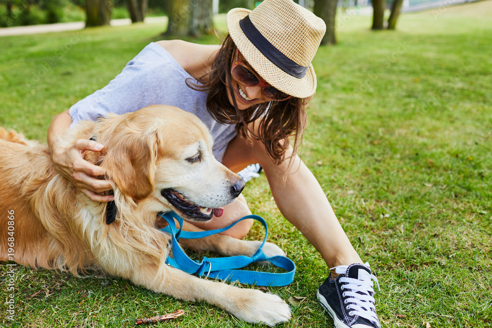 Cheerful young woman petting her dog while sitting on ground in a park Cheerful young woman petting her dog while sitting on ground in a park