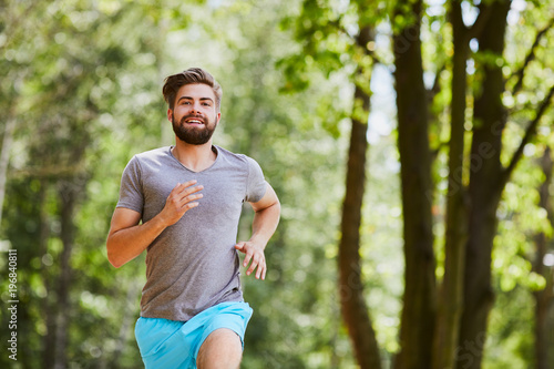 Happy young man jogging outdoors in a park in the summer