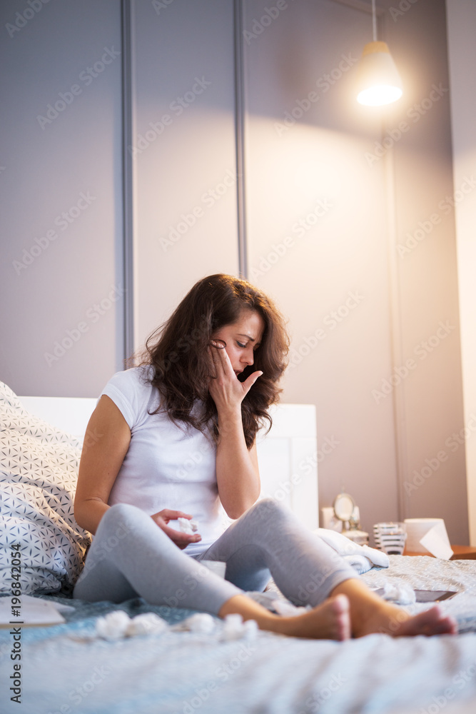 Tired ill middle aged woman holding hands on the cheek while paper wipes are around her on the bed. Tired ill middle aged woman holding hands on the cheek while paper wipes are around her on the bed.