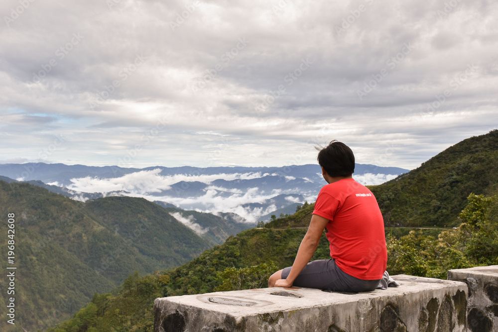 A man looking into the horizon while sitting on the ledge.