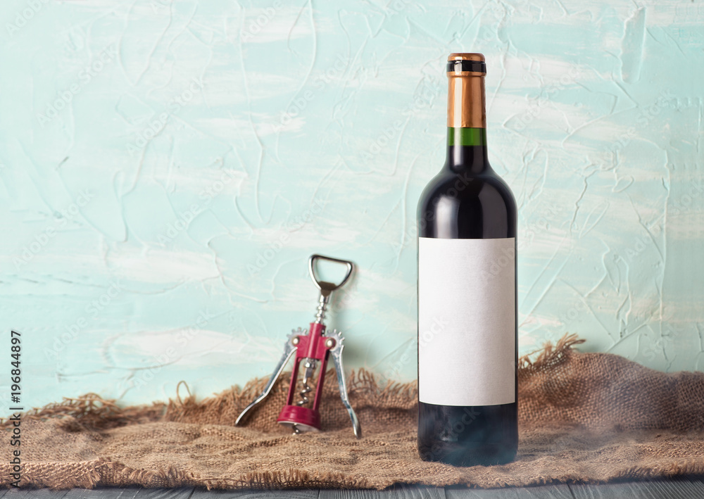 A bottle of red wine with a blank label and a corkscrew on the background