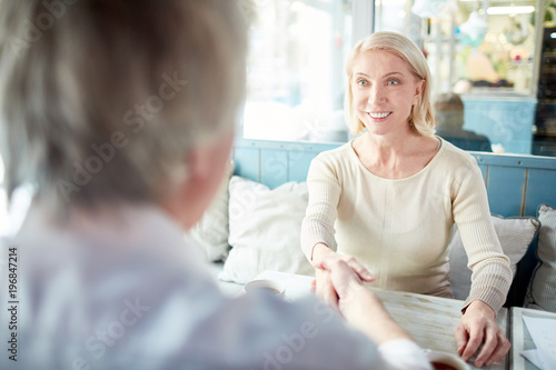 Successful mature businesswoman shaking hand of business partner after signing contract