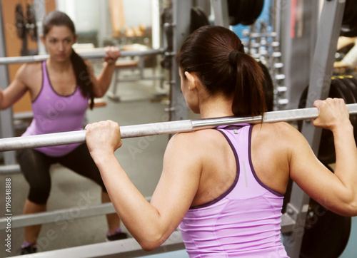 girl gym lifts bar in front mirror