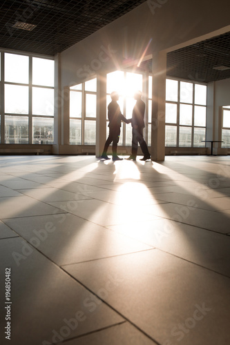 Two business partners shaking hands against window of working area in modern building © pressmaster