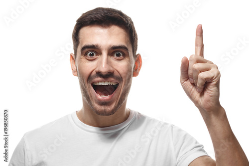 Close up portrait of young handsome smiling man in white t-shirt, pointing his finger in eureka sign, having great innovative idea, understanding solution