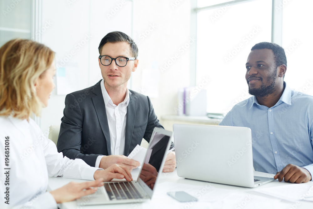 Company of financial analysts or brokers sitting by table and discussing online statistics in office Company of financial analysts or brokers sitting by table and discussing online statistics in office