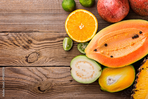 Tropical fruits, papaya, mango, pineapple, passion, guava, lime and orange on wooden background, top view