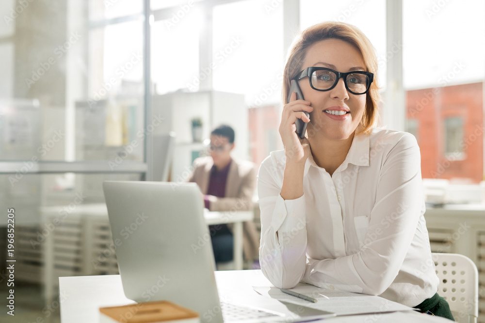 Smiling businesswoman talking on the phone at her workplace Smiling businesswoman talking on the phone at her workplace