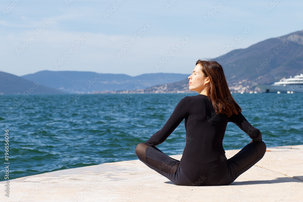 Young girl sitting in yoga lotus meditation position in front to seaside, profile in Montenegrin coast