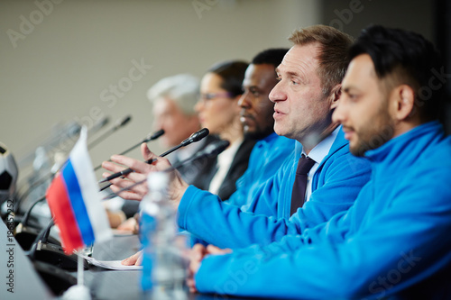 Mature sports trainer talking to microphone while making report for audience