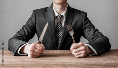 Businessman holding fork with knife and ready to eat. Concept of competition in business photo