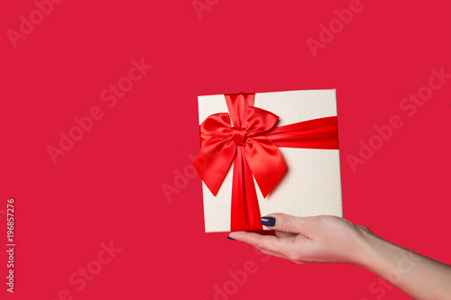 Fototapeta Naklejka Na Ścianę i Meble -  white gift box with a red bow in his hand on a red background.