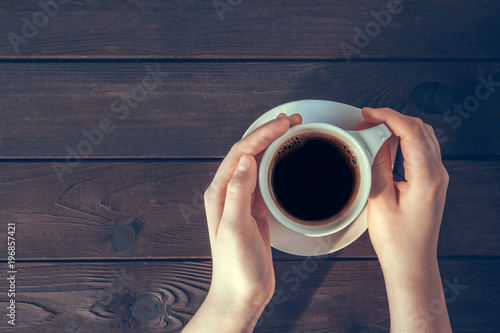 Baby girl hands with a cup of coffee on a wooden background top view flat lay