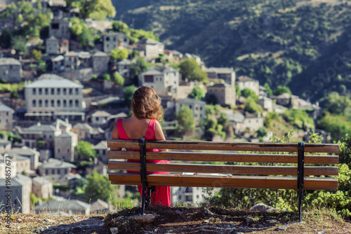 Young female on the bench opposite traditional Village Syrrako in National Park of Tzoumerka, Greece Epirus region