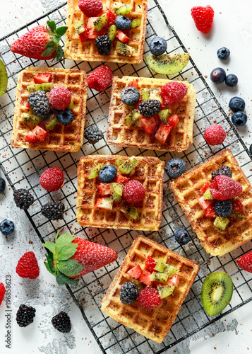 Fresh egg waffles dessert for breakfast with fruits strawberries, blueberries, blackberries, raspberries and kiwi