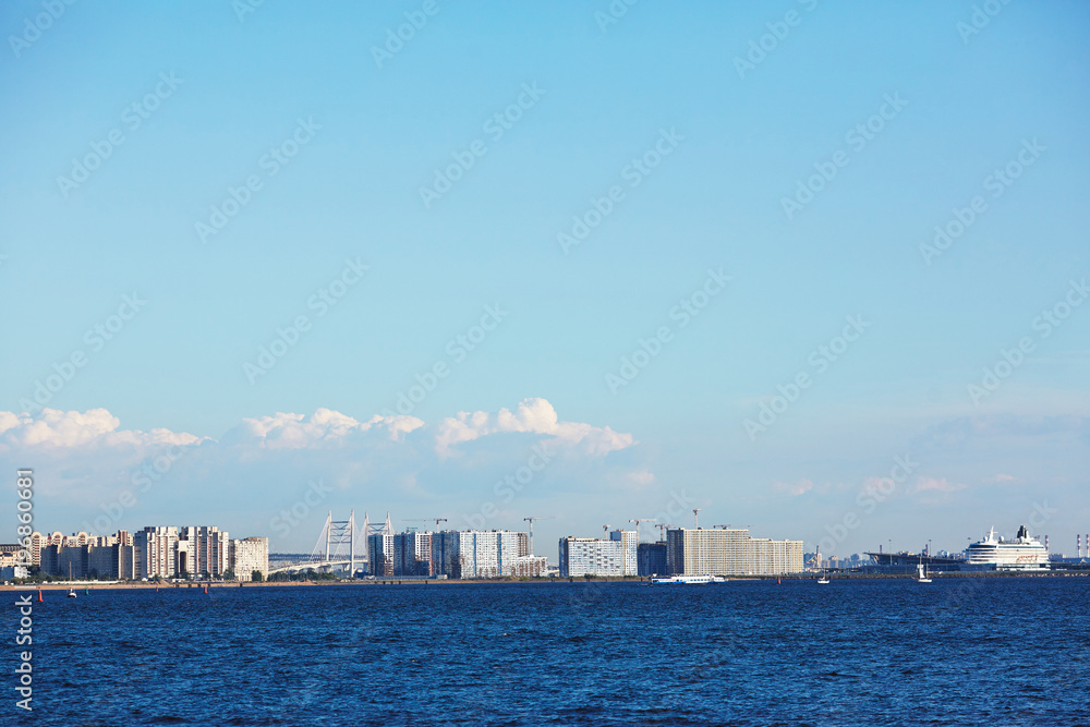 Blue waves of sea and bright sky with cityscape on horizon on hot summer day